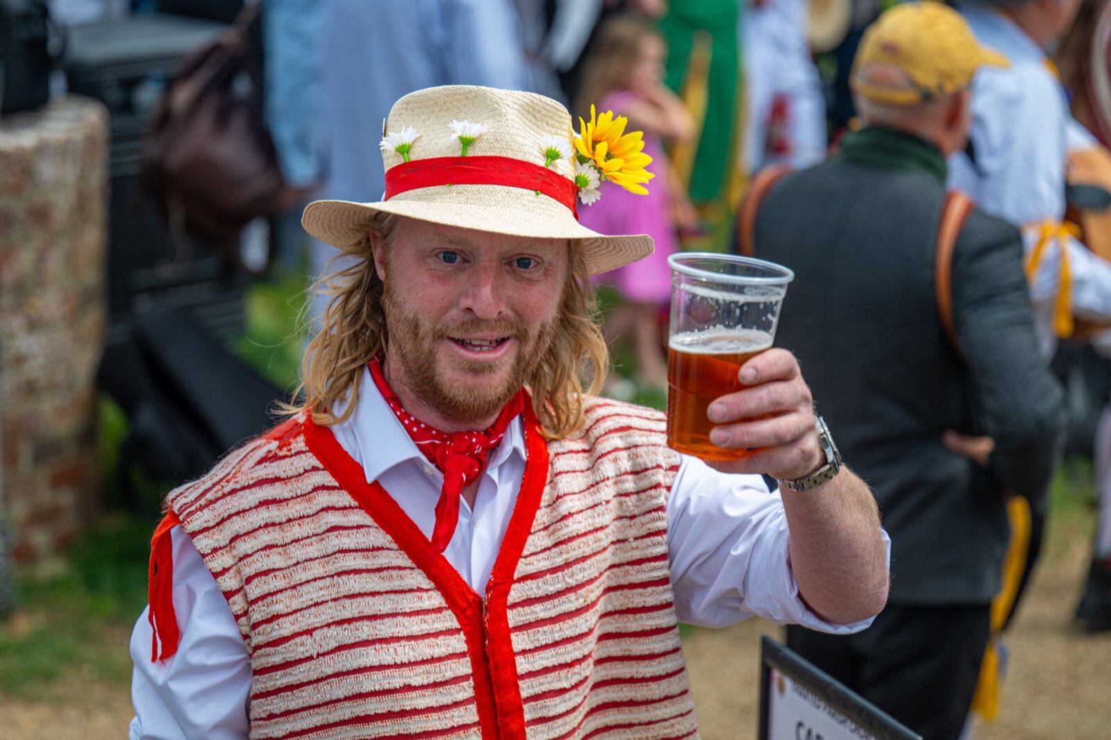 Morris dancer in traditional ribboned dress raising a pint of beer at Thaxted Morris Weekend, Essex